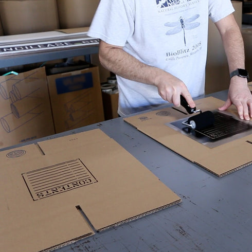Person using a roller over a stencil on cardboard, demonstrating the application of custom magnetic stencils.